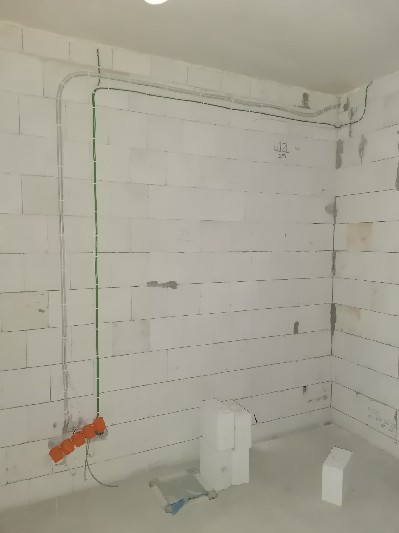 Wewnętrzne okablowanie elektryczne, koryta kablowe i pomarańczowe puszki instalacyjne zamontowane na ścianie z białego bloczka w surowym wnętrzu budynku.