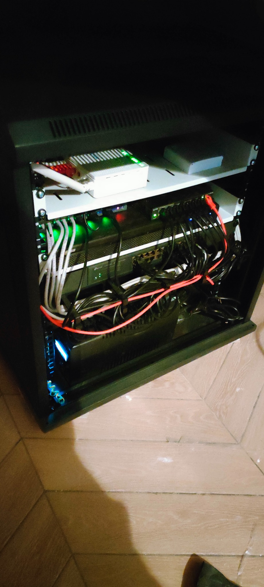 Szafa rack z zainstalowanymi urządzeniami sieciowymi: router, switche, okablowanie UTP, diody LED sygnalizujące pracę urządzeń.