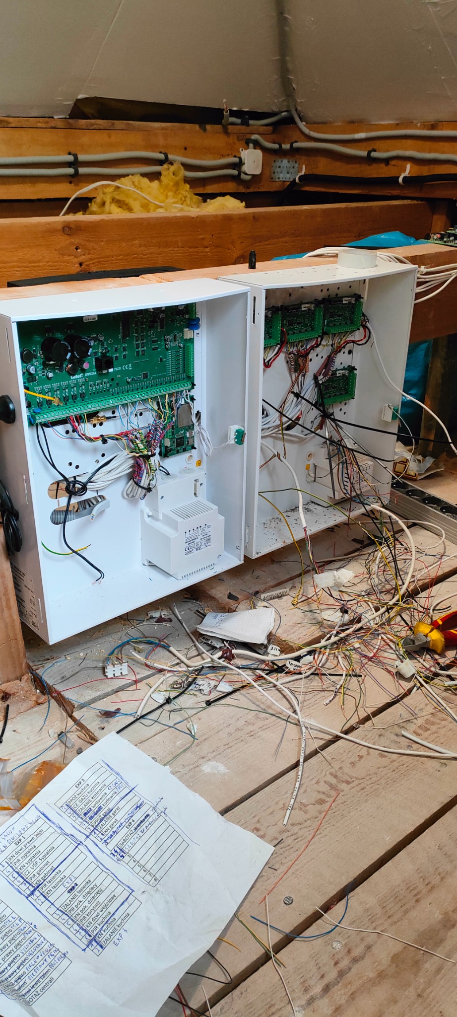 Otwarta szafka sterownicza z widocznymi przewodami i płytkami drukowanymi w trakcie montażu, z rozłożonymi schematami i narzędziami na drewnianej podłodze.
