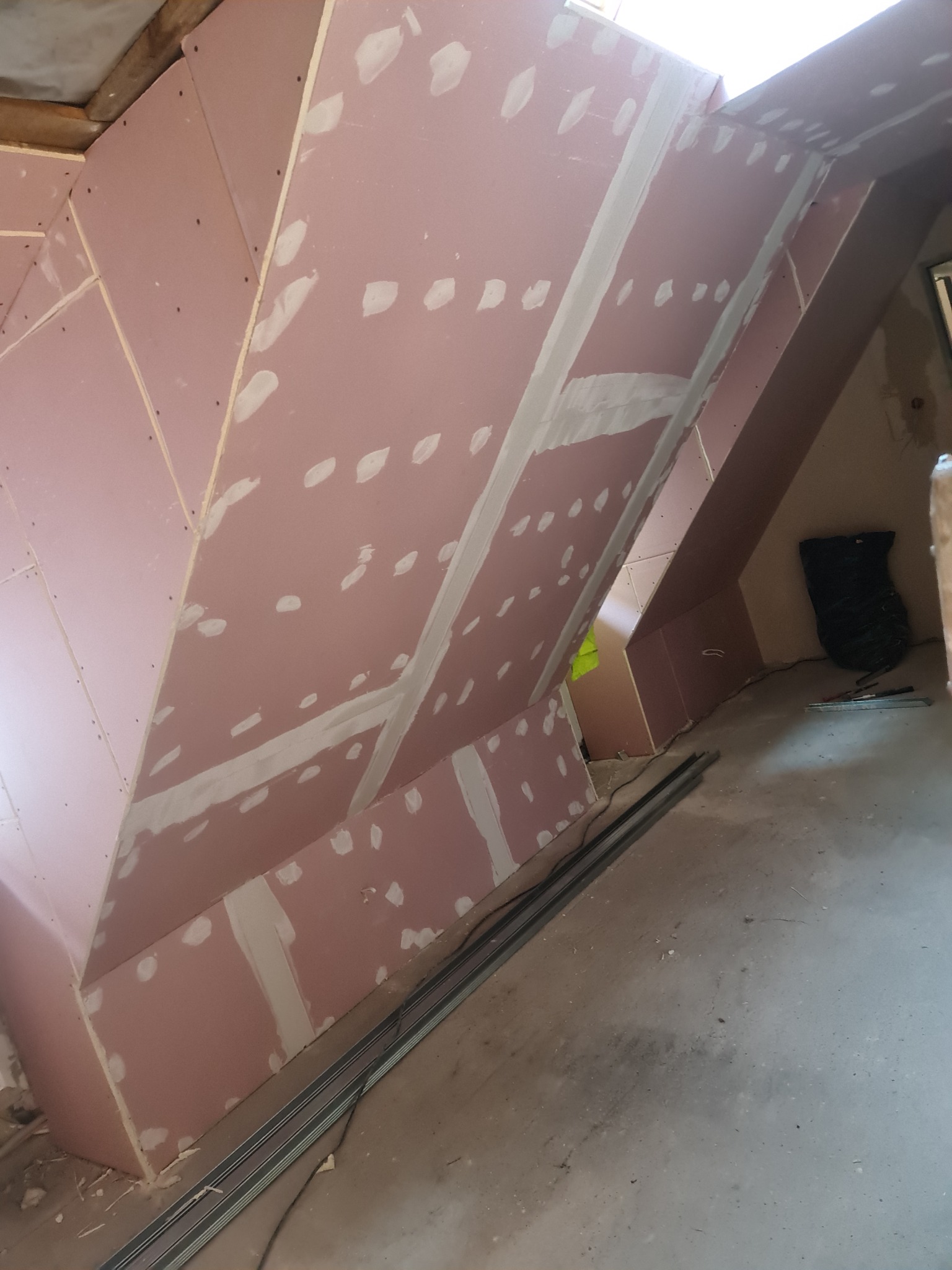 Montaż różowej płyty kartonowo-gipsowej na poddaszu ze szpachlowanymi łączeniami, widoczne profile metalowe i elementy konstrukcyjne dachu.