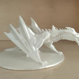 Biała, trójwymiarowa figurka smoka wydrukowana w technologii FDM, stojąca na okrągłej podstawce na drewnianym stole.