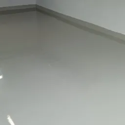 Świeżo wylana, jasnoszara posadzka żywiczna w pomieszczeniu z półką na ścianie, widoczne refleksy światła na gładkiej powierzchni.