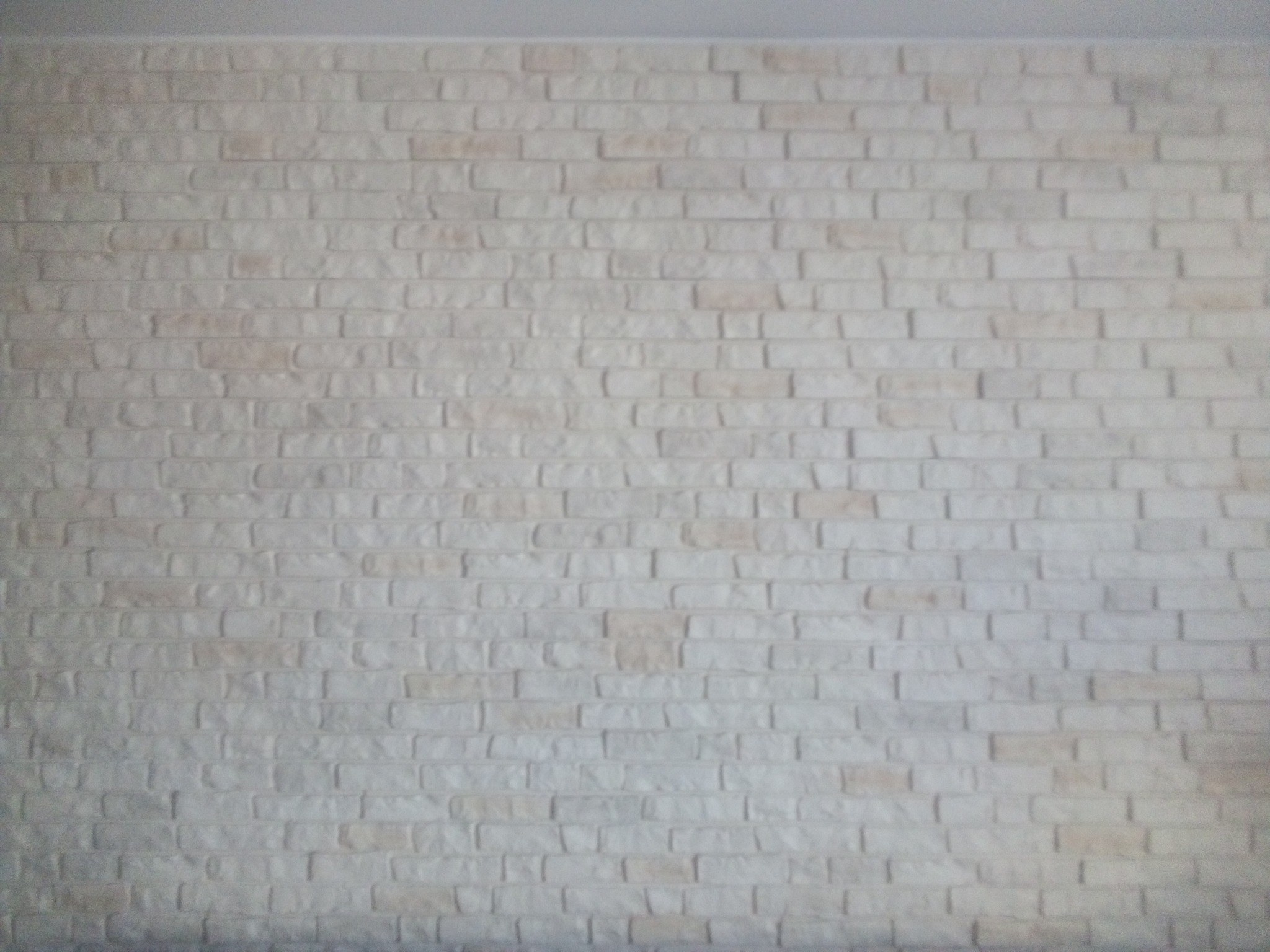 Ściana wyłożona białymi panelami imitującymi cegłę, z widoczną fakturą i nieregularnym ułożeniem.