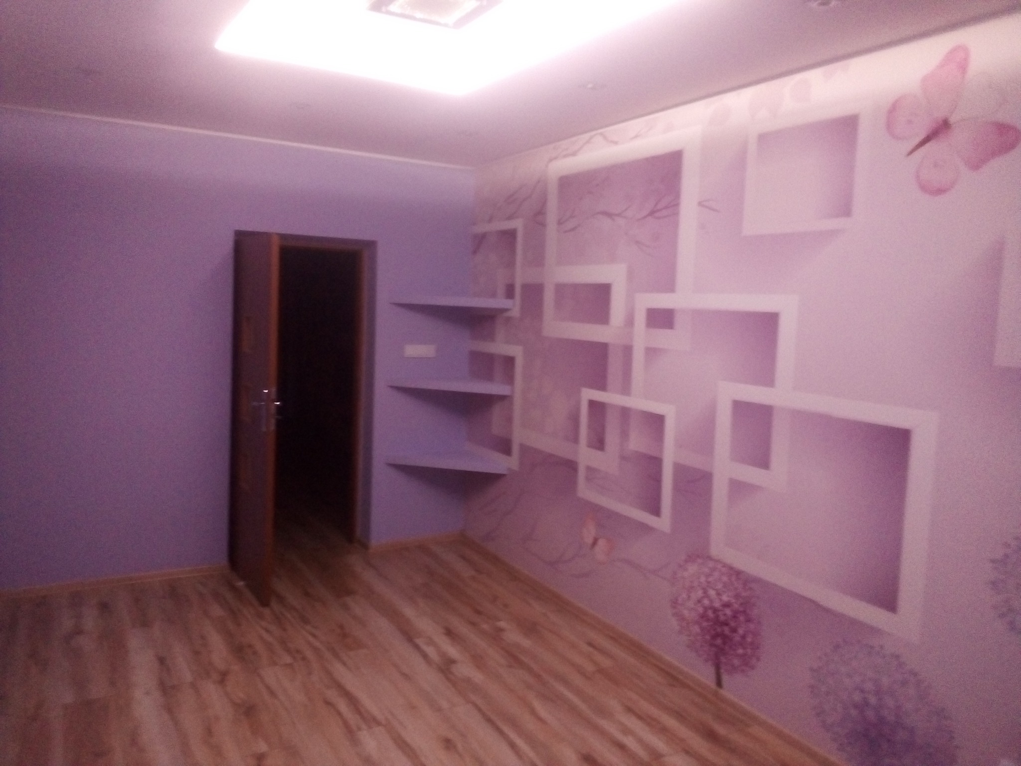 Pokój w odcieniach fioletu z drewnopodobną podłogą, ścianą z tapetą w geometryczne wzory i motywem motyla, oraz otwartymi półkami na ścianie.