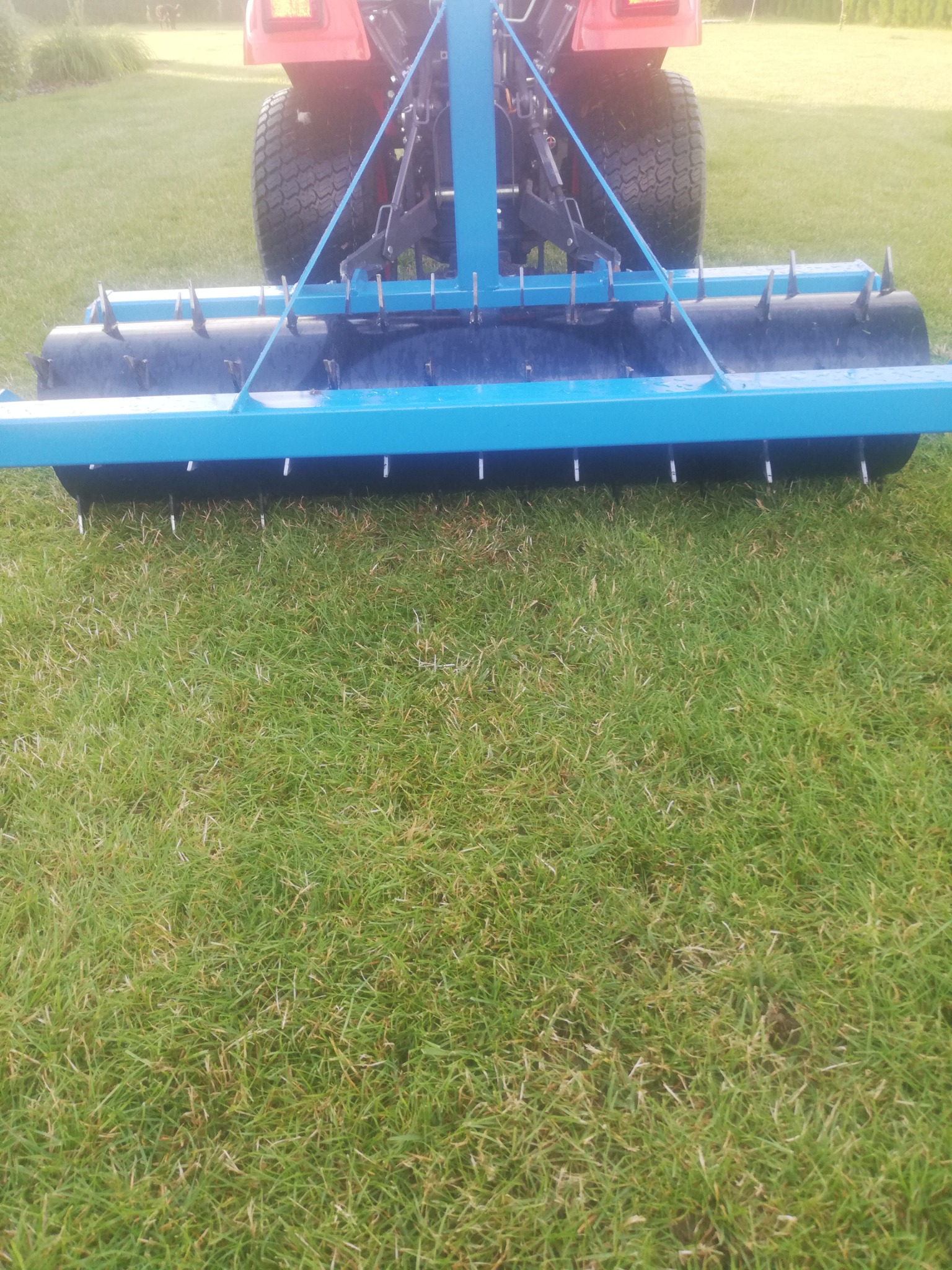 Aerator do trawy podłączony do traktorka na tle zielonego trawnika