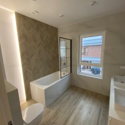 Retro - Nowoczesna łazienka z wanną z czarną ramą kabiny, umywalką nablatową i podświetloną ścianą z wzorem jodełki, drewnopodobna podłoga z płytek.