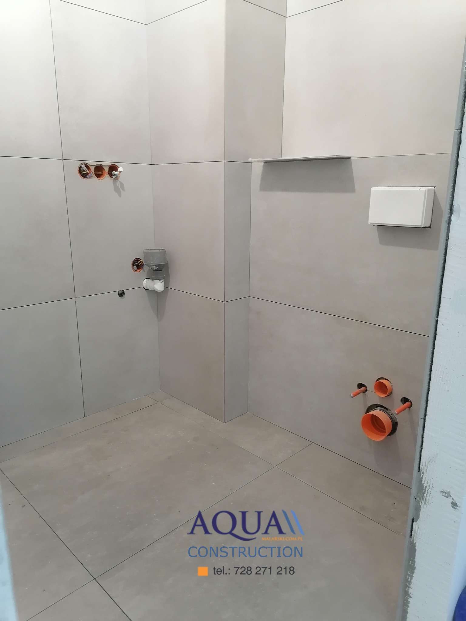 Wnętrze łazienki w trakcie remontu z położonymi jasnymi płytkami na ścianach i podłodze, widoczne instalacje wodno-kanalizacyjne oraz logo firmy Aqua Construction w dolnej części kadru.