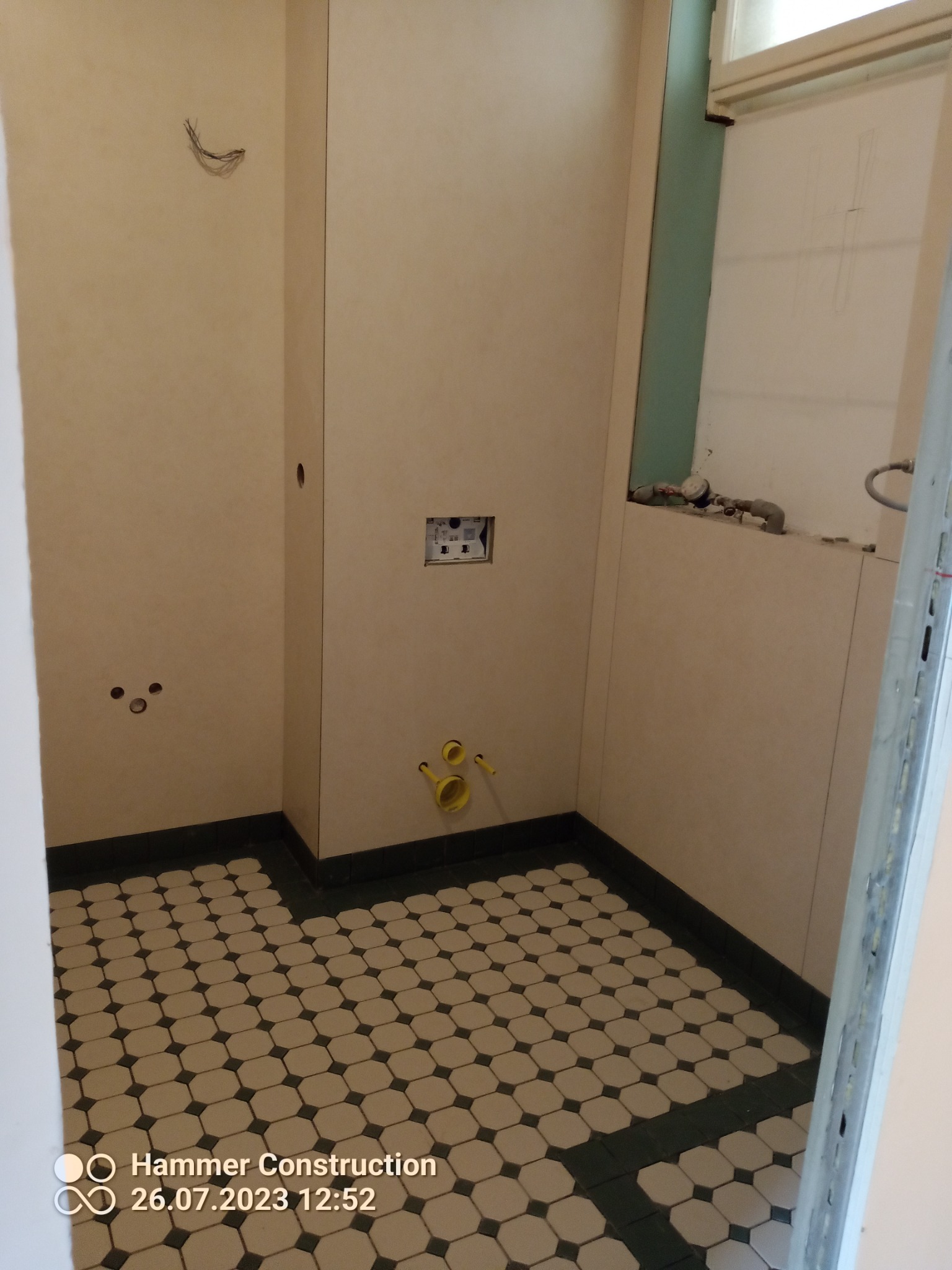 Łazienka w trakcie remontu: widoczne płytki podłogowe w stylu retro, przygotowane ściany z wystającymi przewodami elektrycznymi i rurami hydraulicznymi przed montażem armatury.