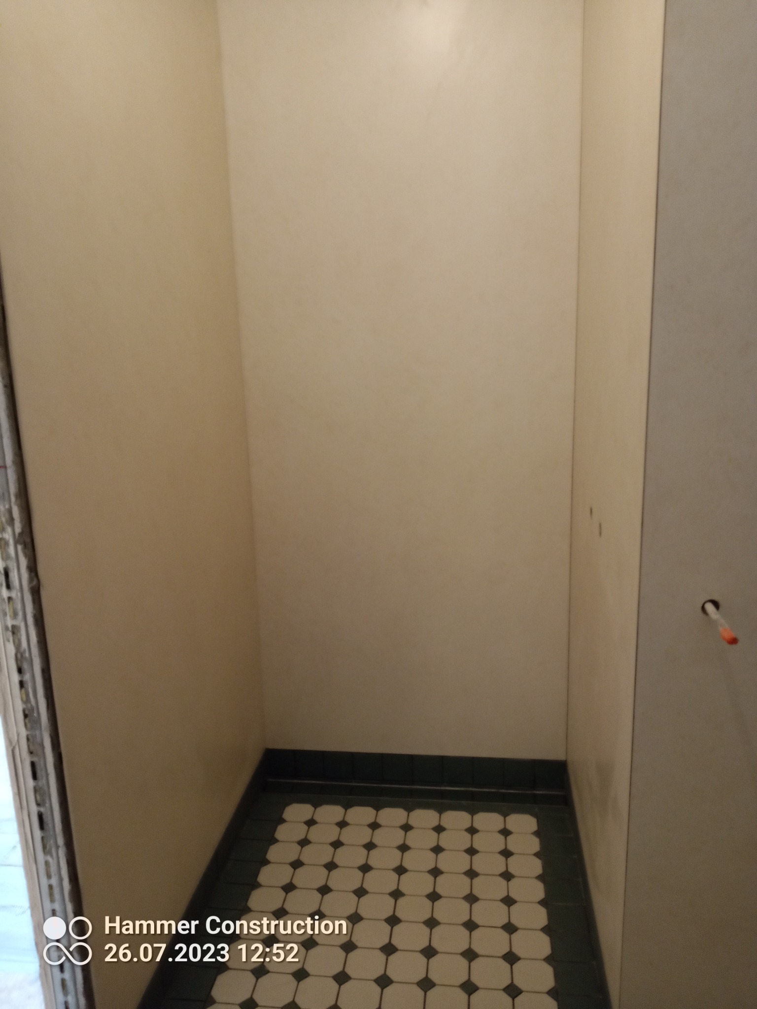 Fragment łazienki po remoncie: kremowe ściany i podłoga z płytek w biało-czarne romby z ciemnozieloną obwódką.