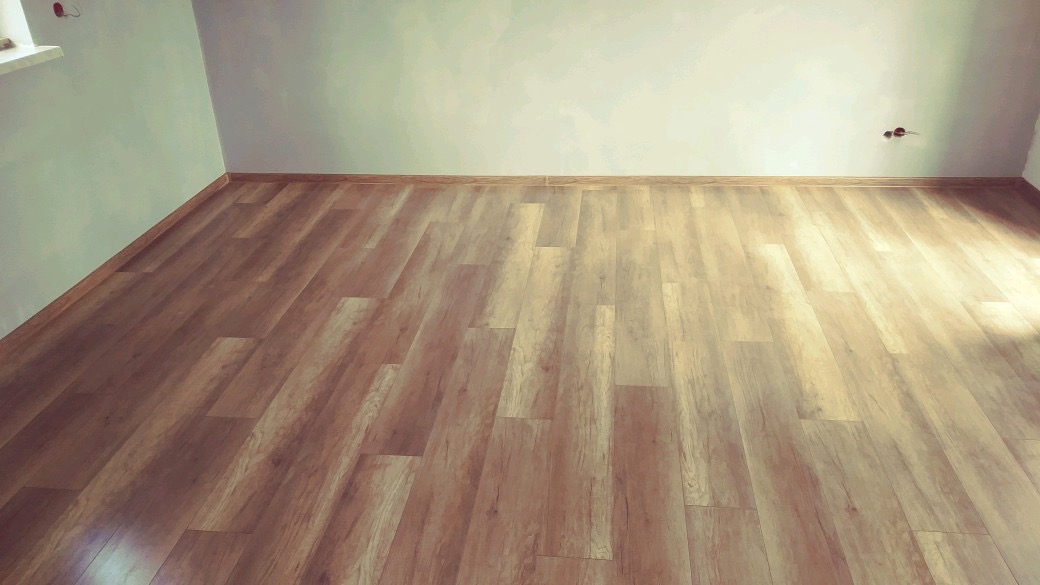 Ułożone panele podłogowe w nowym pomieszczeniu z widocznymi gniazdkami elektrycznymi i listwami przypodłogowymi.