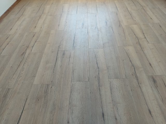 Jasne panele podłogowe imitujące drewno z wyraźnym rysunkiem słojów, ułożone wzdłuż pokoju.