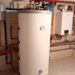 Bojler akumulacyjny z termometrem, piec gazowy Vaillant, instalacja z rur miedzianych i plastikowych w pomieszczeniu wyłożonym płytkami.