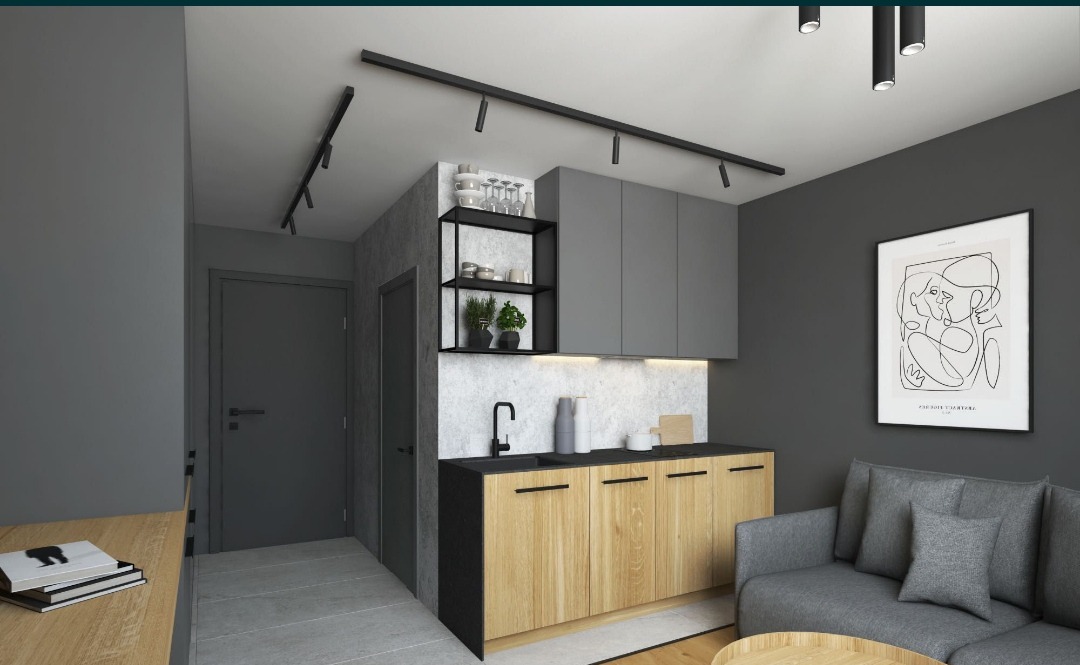 Nowoczesna aranżacja małej kuchni z drewnianymi szafkami dolnymi, szarymi szafkami górnymi, czarnym blatem i armaturą, oświetleniem szynowym oraz minimalistycznym plakatem na ścianie w szarym kolorze.