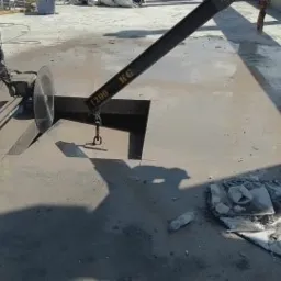 Cięcie betonu piłą diamentową na mokro, operator w kamizelce odblaskowej, widoczne fragmenty odciętej płyty i urządzenie podwieszone na dźwigu.