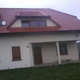 Dom jednorodzinny z nowym, czerwonym dachem z dachówki ceramicznej i oknem dachowym, widok z poziomu trawnika.