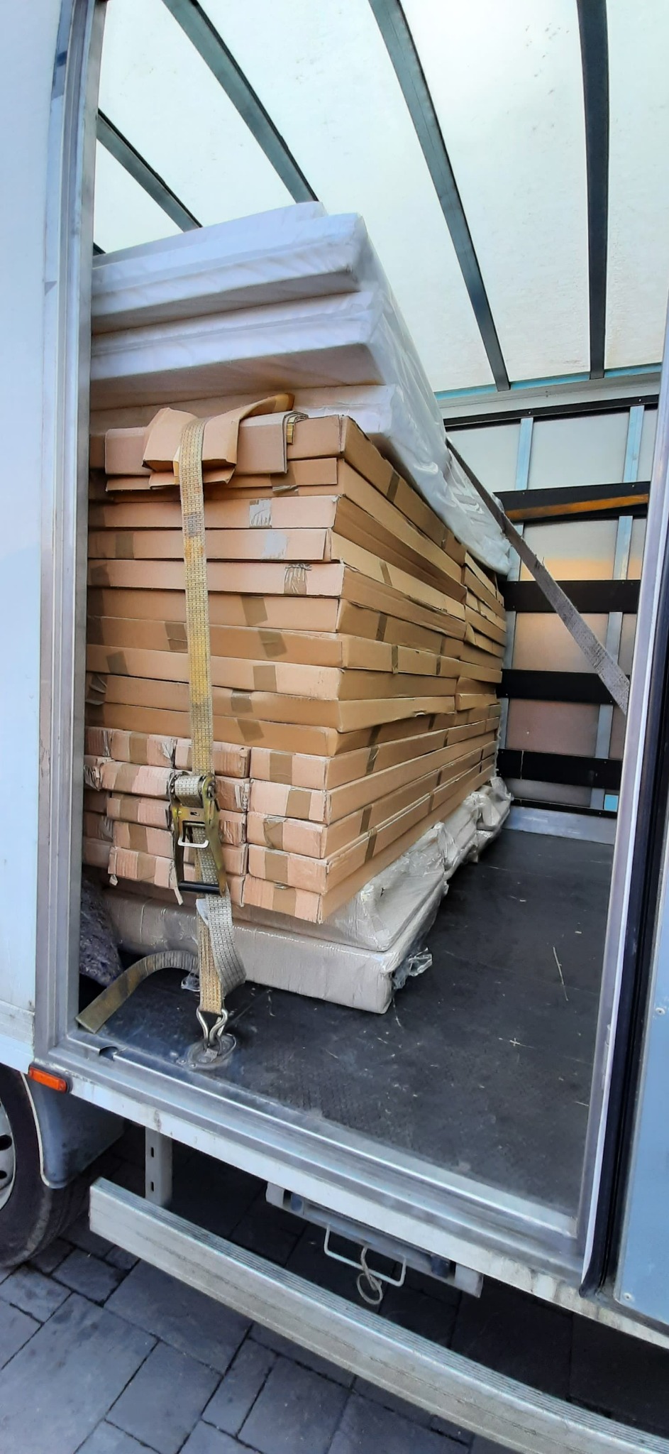 Wnętrze furgonetki wypełnione po brzegi kartonami i meblami zabezpieczonymi pasami transportowymi, gotowe do przewozu.