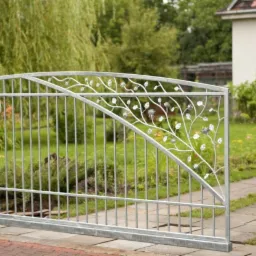 Otwarta, metalowa brama wjazdowa z dekoracyjnym motywem roślinnym w postaci gałązek z liśćmi, wykonana z surowego metalu, widok na zielony ogród i dom w tle.