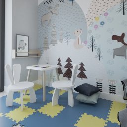 UJMA Architekci Justyna Ujma - Pokój dziecięcy z białym stolikiem, krzesłami w kształcie króliczych uszu i tapetą w leśne zwierzęta, uzupełniony o poduszki i fragment łóżka z szarą pościelą.