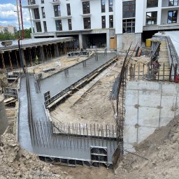 DGP - SPÓŁKA Z OGRANICZONĄ ODPOWIEDZIALNOŚCIĄ - Wylany beton w szalunkach pod fundamenty budynku wielorodzinnego, widoczna zbrojenie i pompa do betonu w tle.
