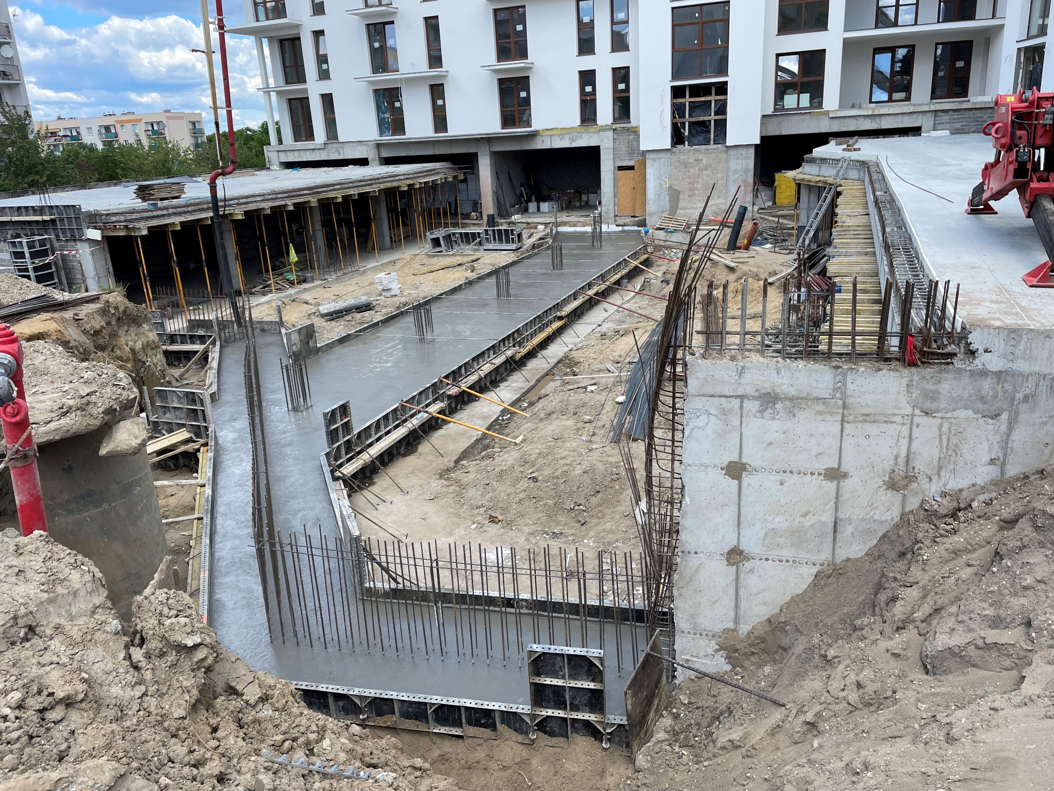 Wylany beton w szalunkach pod fundamenty budynku wielorodzinnego, widoczna zbrojenie i pompa do betonu w tle.