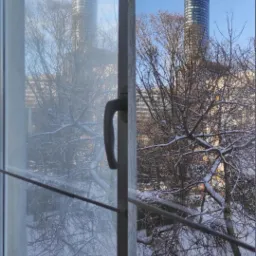 Okno po lewej stronie brudne, po prawej czyste, widok na zaśnieżone drzewa i wieżowiec w tle w słoneczny dzień.