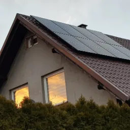 Panele słoneczne na dachu domu jednorodzinnego w Szczecinie, odbicie zachodzącego słońca w oknach.