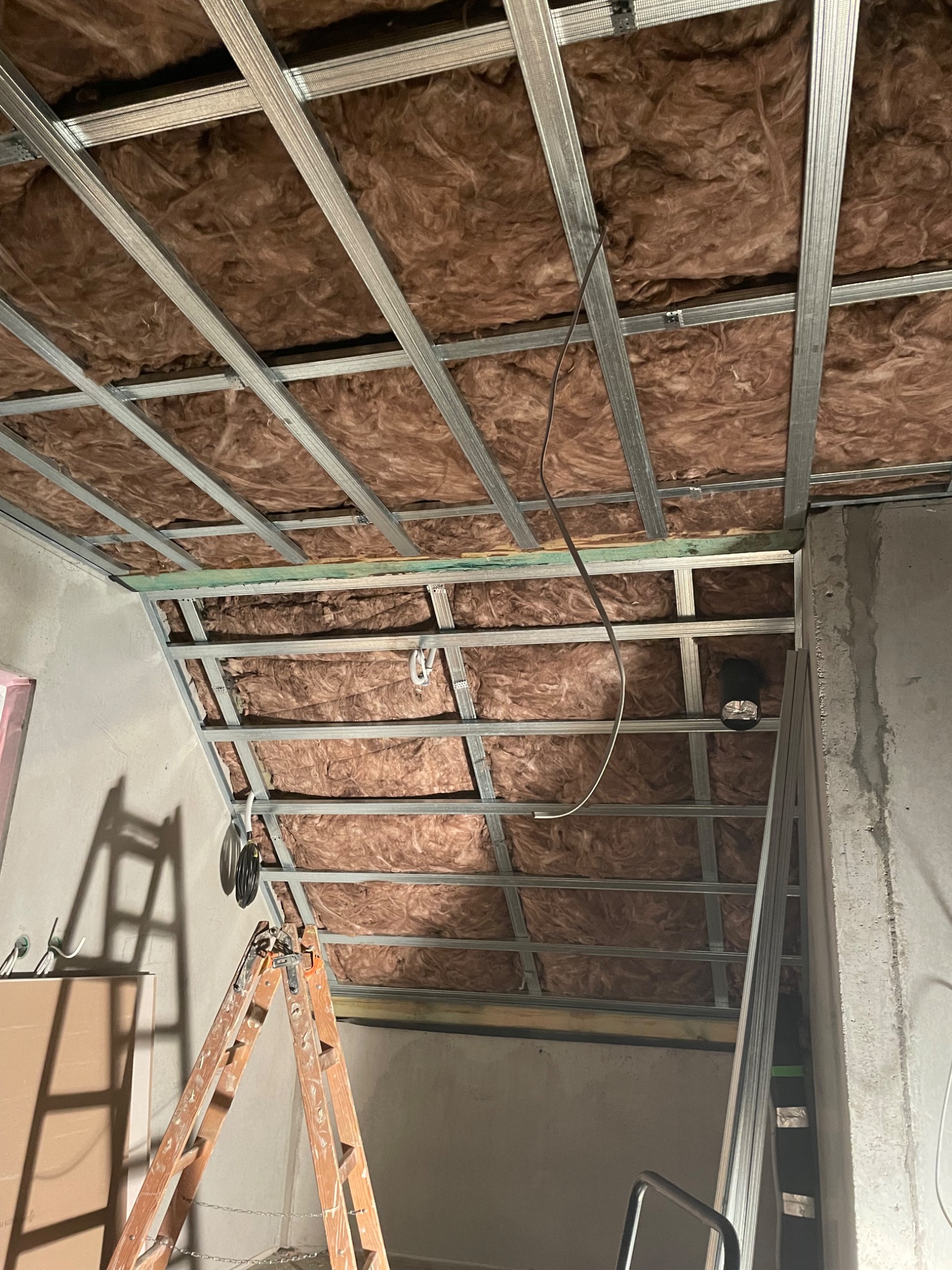 Poddasze w trakcie ocieplania wełną mineralną, widoczna metalowa konstrukcja szkieletowa i drabina oparta o ścianę.