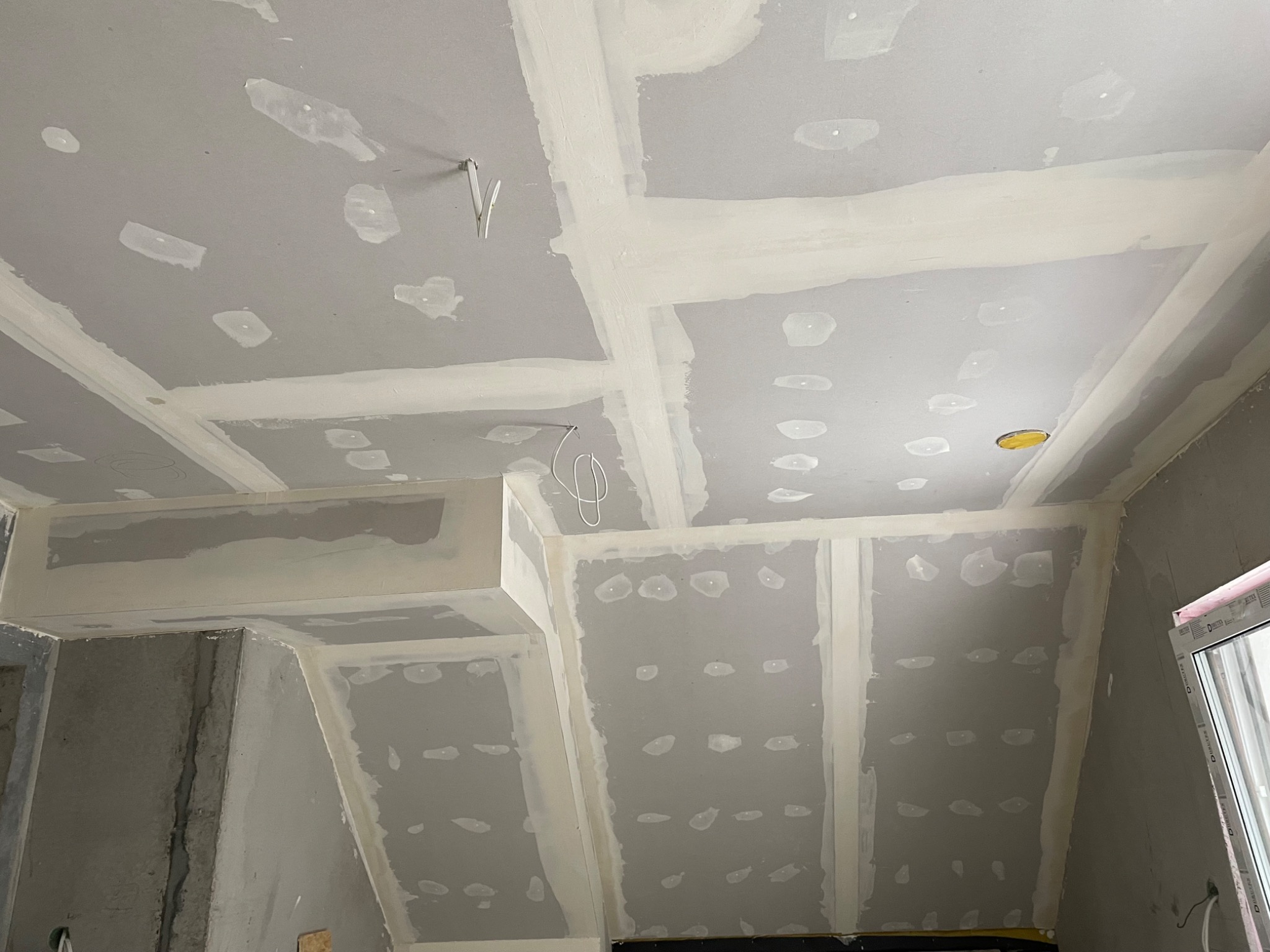 Sufit i ściany poddasza po montażu płyt gipsowo-kartonowych, z widocznymi łączeniami wypełnionymi masą szpachlową, przed szlifowaniem i malowaniem, z wystającymi przewodami elektrycznymi.