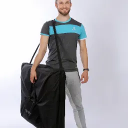 Uśmiechnięty mężczyzna w sportowym stroju pozuje z torbą na przenośny stół do masażu w Poznaniu, widoczny napis 'YENIlife' na torbie.