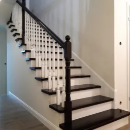 Dwukolorowe schody wewnętrzne z ciemnego drewna i białych elementów, widok z dołu, z drewnianą podłogą w tle.