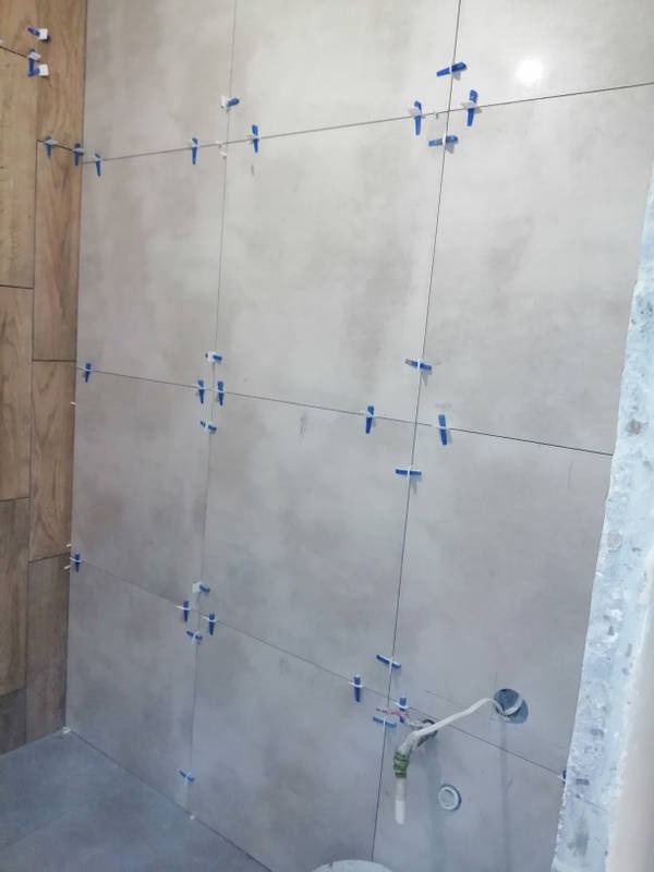 Świeżo ułożone, jasnoszare płytki na ścianie łazienki w Pabianicach, z widocznymi krzyżykami dystansowymi i poziomymi sznurkami wyznaczającymi linie fug. Przygotowane otwory na instalacje.