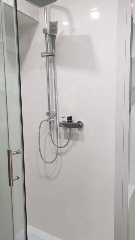 Nowoczesna kabina prysznicowa z deszczownicą i baterią termostatyczną, wykończona białymi, prostokątnymi płytkami.