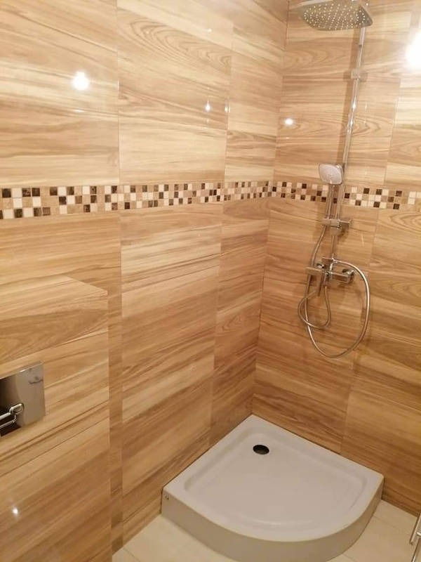 Nowoczesna kabina prysznicowa z drewnopodobnymi płytkami ceramicznymi, dekoracyjnym pasem mozaiki i minimalistyczną armaturą.