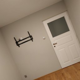 Silver Hands - Ściana w pokoju po malowaniu z zamontowanym uchwytem do telewizora i białe drzwi z szybą.