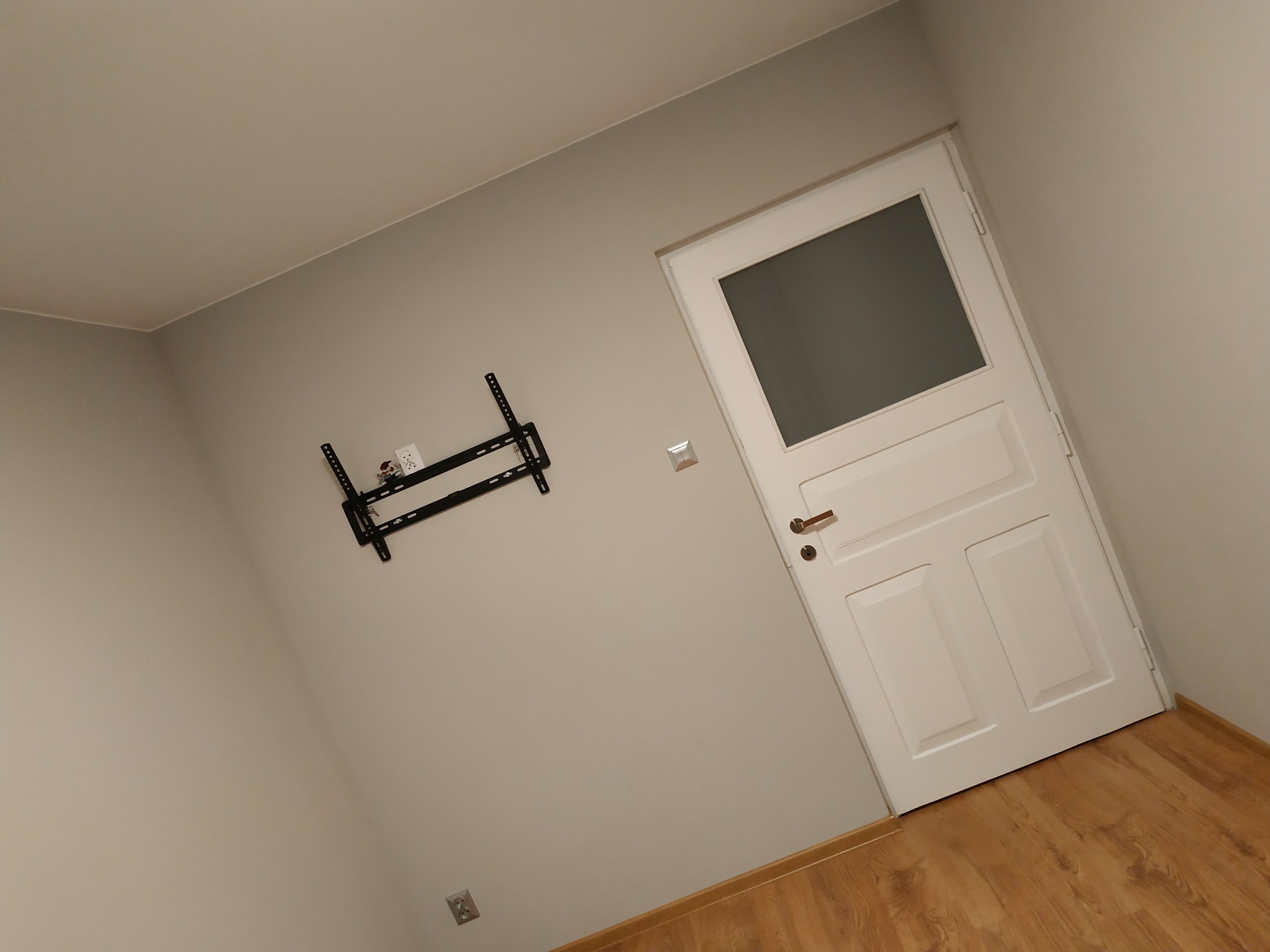 Ściana w pokoju po malowaniu z zamontowanym uchwytem do telewizora i białe drzwi z szybą.