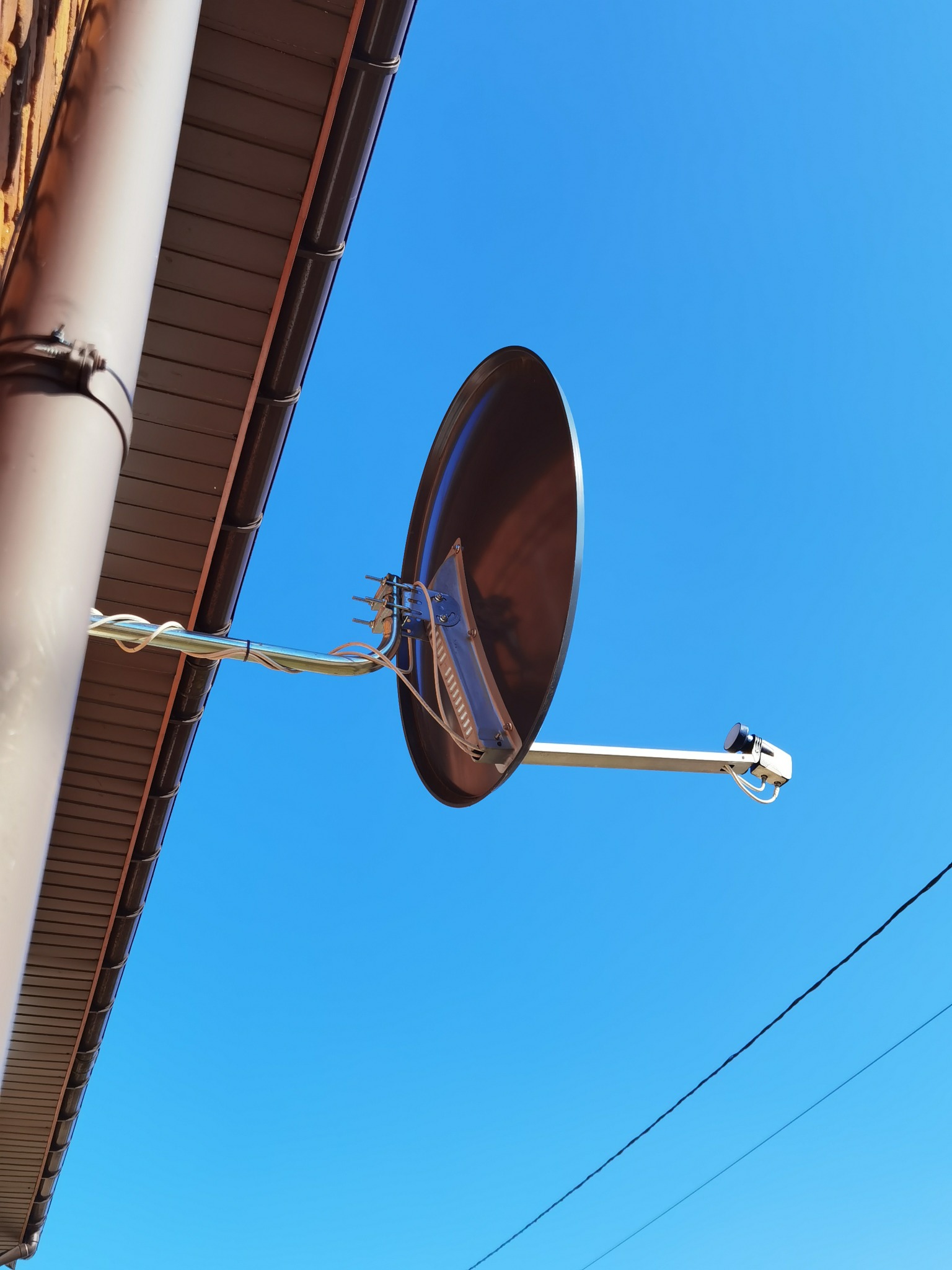 Antena satelitarna zamocowana do ściany budynku, widoczna na tle błękitnego nieba. Kabel antenowy schludnie przymocowany do wspornika.
