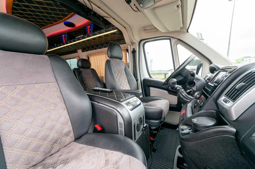 Wnętrze luksusowo wykończonego busa z pikowanymi skórzanymi siedzeniami, oświetleniem LED i panelem sterowania multimediami.