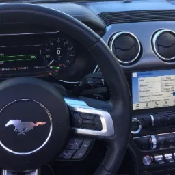 Wnętrze samochodu z widocznym kokpitem, kierownicą z logo konia, ekranem dotykowym ustawionym na język polski i panelem klimatyzacji.