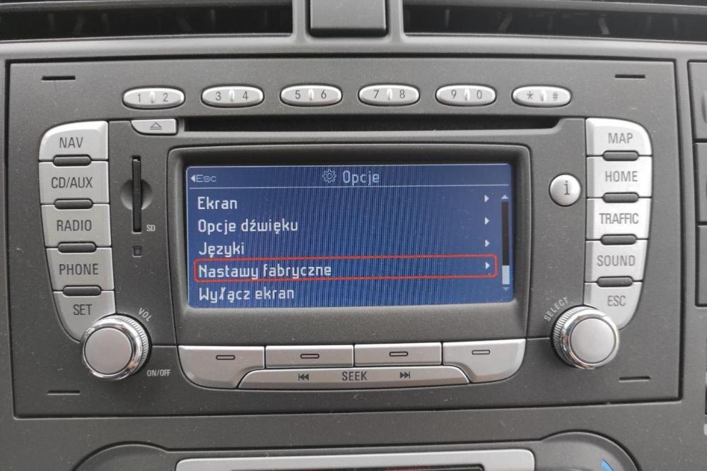 Wyświetlacz samochodowego systemu multimedialnego z menu ustawień fabrycznych zaznaczonym na czerwono.