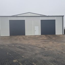 BPJA Paweł Bernacki - Nowoczesny budynek magazynowy z dwoma szarymi bramami segmentowymi i białymi panelami elewacyjnymi, widok zewnętrzny w pochmurny dzień.