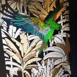 Ściana z ręcznie malowanym muralem przedstawiającym tropikalny motyw z papugą w locie, wykonana w czerni, bieli, brązach i odcieniach zieleni i błękitu.
