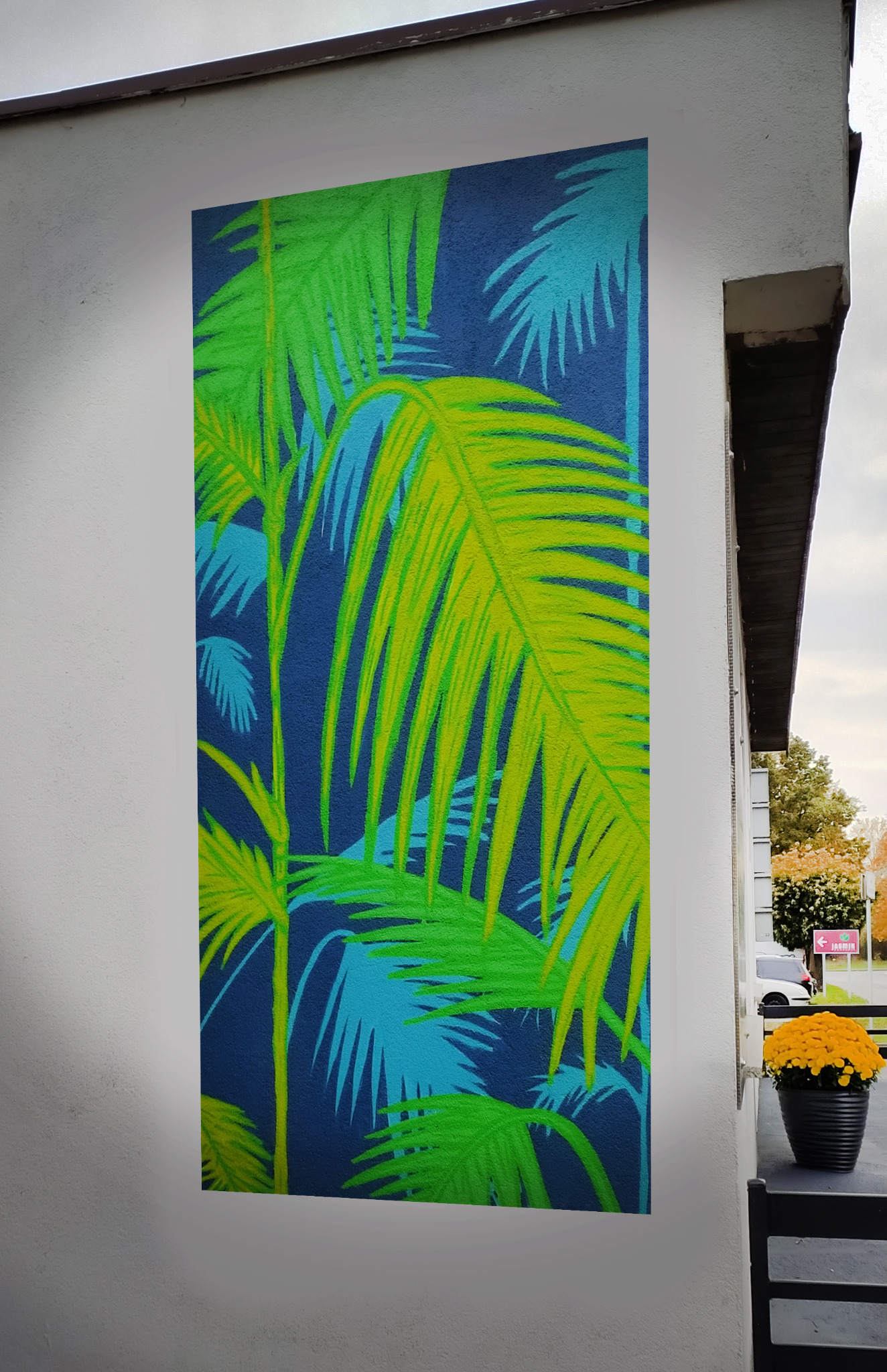 Duży mural z motywem tropikalnych liści palmowych w odcieniach zieleni i błękitu na ciemnoniebieskim tle, umieszczony na białej ścianie budynku z widoczną donicą z żółtymi kwiatami w tle.