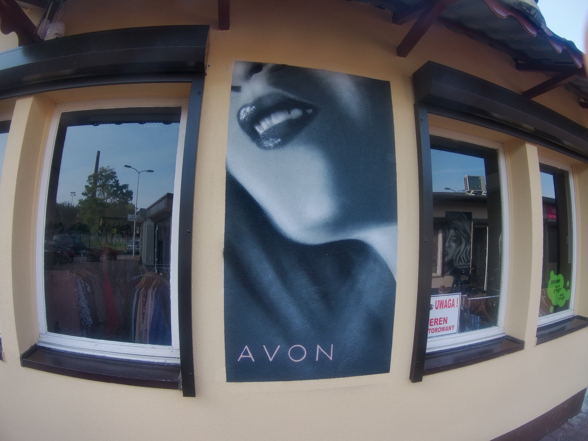 Zewnętrzna ściana budynku z oknami i plakatem Avon przedstawiającym zbliżenie ust z błyszczącymi zębami.