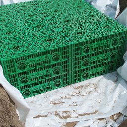 HYDROREM - Zielony, modułowy system drenażowy Pipe Life, ułożony w wykopie wyłożonym białą geowłókniną, otoczony ziemią i przygotowany do zasypania.