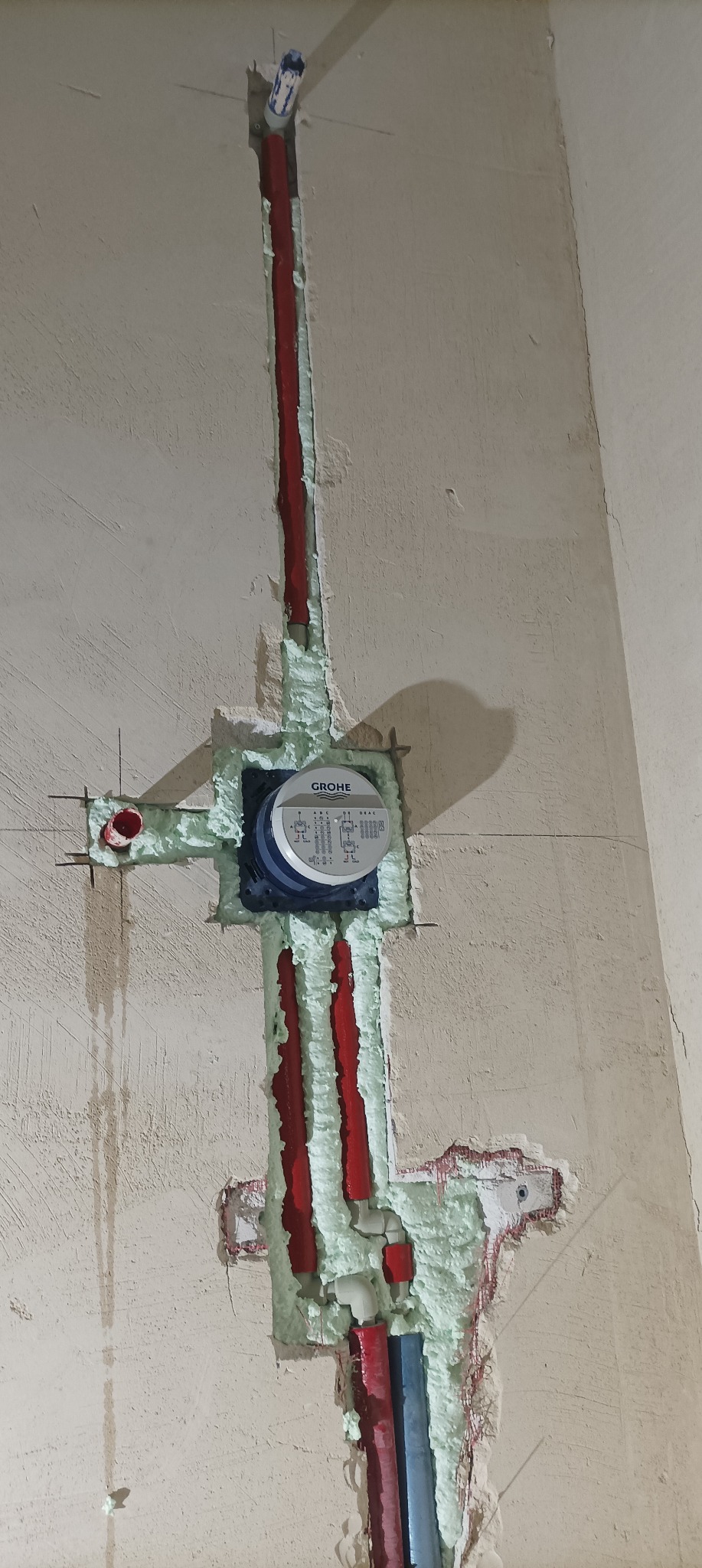 Montaż wodomierza marki Grohe w ścianie z wypełnionymi pianką instalacjami hydraulicznymi w trakcie remontu w Ostrowie Wielkopolskim.