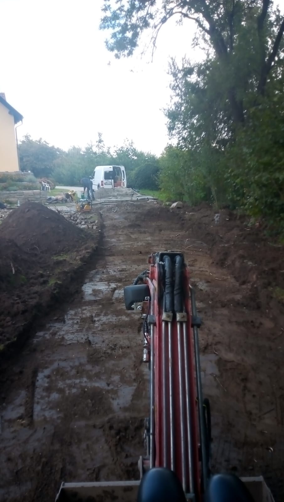 Widok z kabiny minikoparki podczas prac ziemnych we Wrocławiu, w tle widoczny pracownik i samochód dostawczy na przygotowanym terenie.