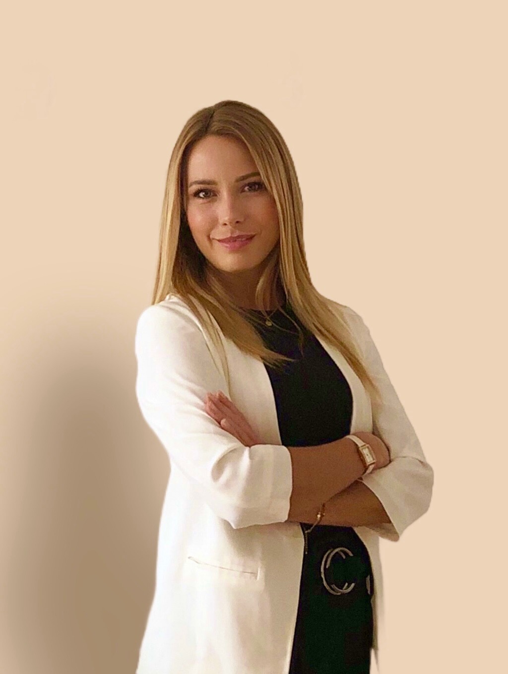 Portret uśmiechniętej kobiety w białej marynarce, z założonymi rękoma, na jednolitym tle.