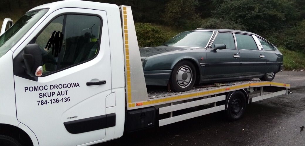 Citroen CX Turbo na platformie pomocy drogowej; na drzwiach białego pojazdu numer telefonu 784-136-136; widok z boku.