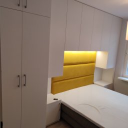 Zakład Produkcji Mebli i Usług Budowlano Transportowych AL-JA Alfons Labuda - Biała szafa na wymiar zintegrowana z zabudową łóżka, żółty tapicerowany zagłówek z oświetleniem LED, minimalistyczny design.