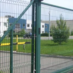 Przesuwna brama panelowa z automatyczną blokadą, widok z zewnątrz na tle budynków biurowych i zielonego trawnika.